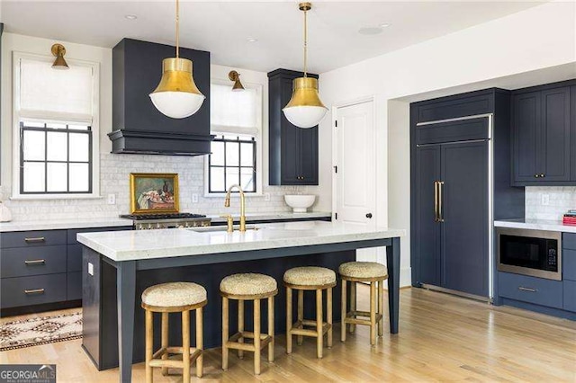 kitchen featuring light wood-style floors, a kitchen breakfast bar, a sink, decorative backsplash, and built in appliances