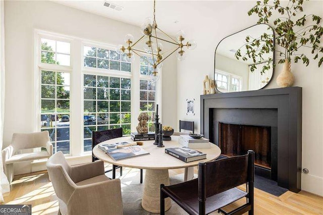 dining room featuring a chandelier, a fireplace with flush hearth, visible vents, and light wood-style floors