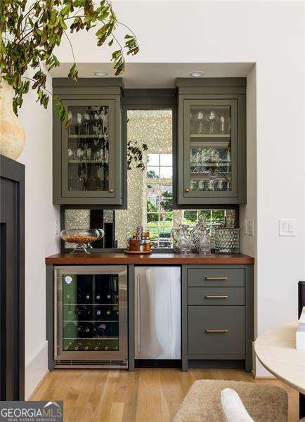 bar featuring tasteful backsplash, stainless steel fridge, a dry bar, light wood-style floors, and wine cooler