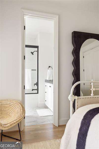 bedroom with light wood-type flooring, baseboards, and connected bathroom
