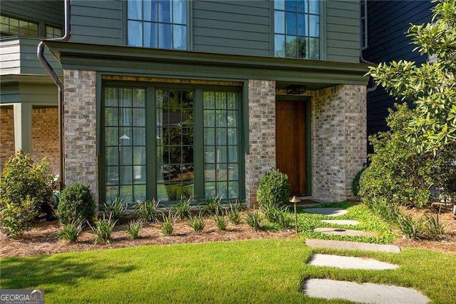 view of exterior entry with a yard and brick siding