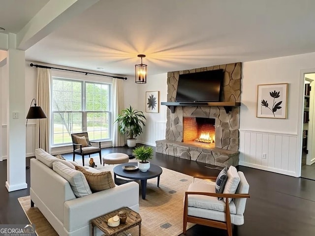 living room featuring a stone fireplace, wood finished floors, and a wainscoted wall