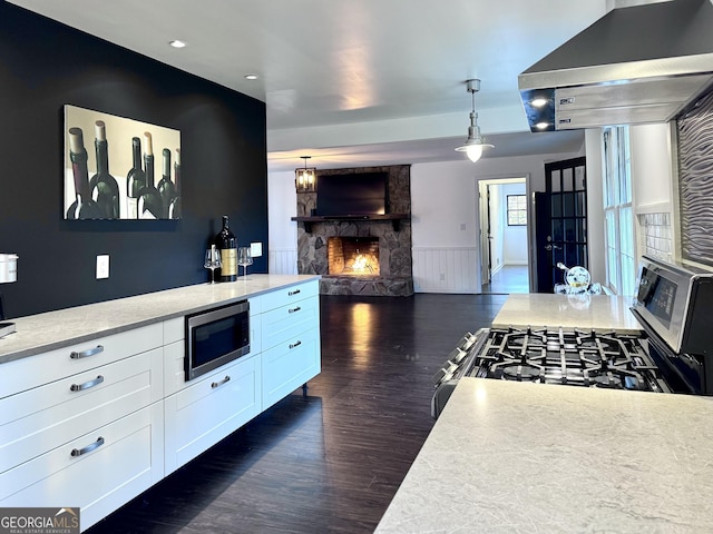 kitchen with wall chimney exhaust hood, white cabinetry, a fireplace, dark wood-type flooring, and appliances with stainless steel finishes