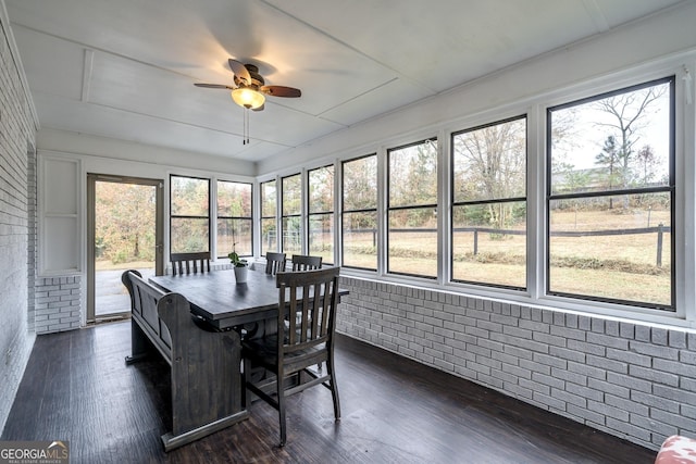 sunroom with ceiling fan, a healthy amount of sunlight, outdoor dining space, and brick wall