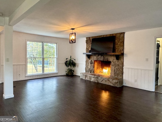 living room featuring wainscoting, dark wood finished floors, and a stone fireplace