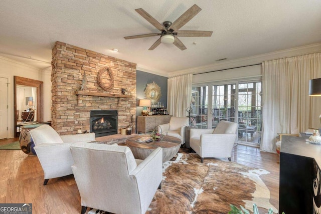 living area with crown molding, wood finished floors, ceiling fan, a stone fireplace, and a textured ceiling