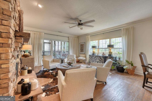 living room with ceiling fan, ornamental molding, a textured ceiling, wood finished floors, and baseboards