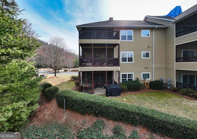 rear view of house featuring a sunroom, a balcony, a yard, and a chimney