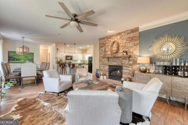 living area with light wood-style floors, ceiling fan, a chandelier, ornamental molding, and a stone fireplace