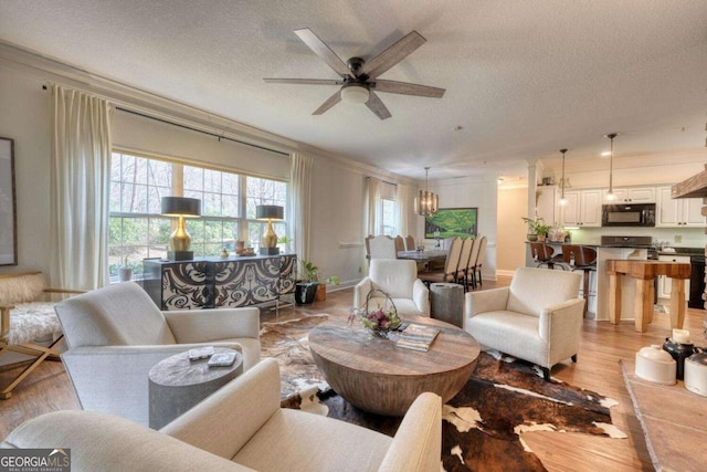living room featuring light wood-type flooring, a chandelier, a textured ceiling, ceiling fan, and ornamental molding