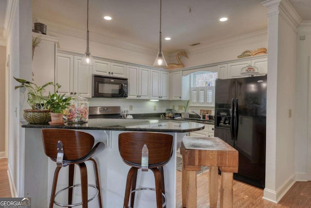 kitchen featuring black appliances, a breakfast bar, a peninsula, light wood-type flooring, and hanging light fixtures