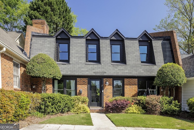 view of front of property with brick siding, a front lawn, a chimney, and a shingled roof