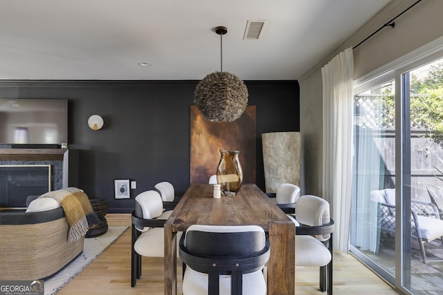 dining space featuring light wood-style floors, a glass covered fireplace, visible vents, and crown molding