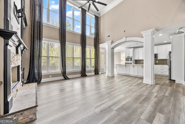 774 Mary Ann Dr NE, Marietta, GA 30068 - unfurnished living room with crown molding, light wood-style floors, ceiling fan, ornate columns, and a stone fireplace