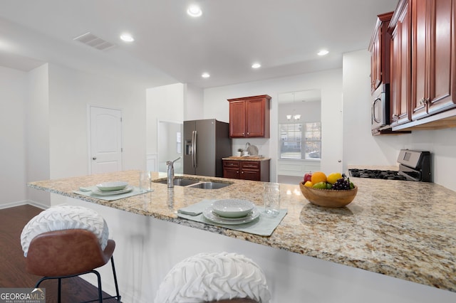 kitchen featuring stainless steel appliances, dark brown cabinets, light stone counters, a breakfast bar area, and a peninsula
