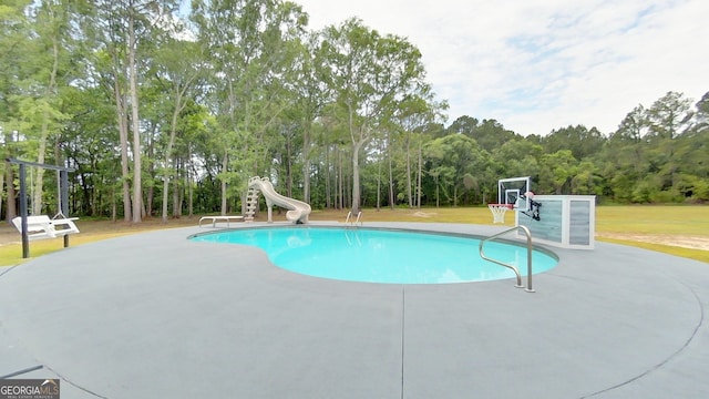 outdoor pool with a water slide, a lawn, a diving board, and a patio