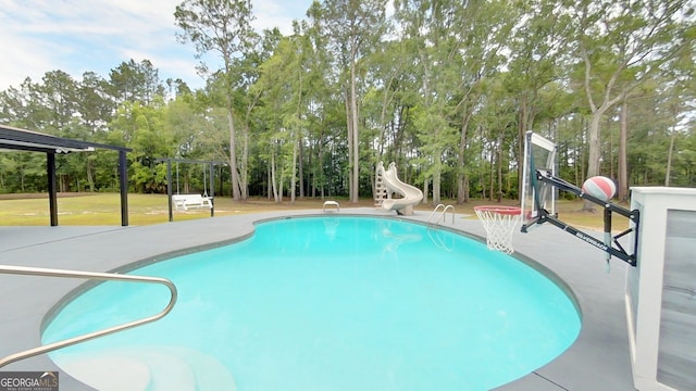 outdoor pool with a water slide and view of wooded area