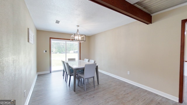 dining space featuring light wood-type flooring, a chandelier, baseboards, and beam ceiling