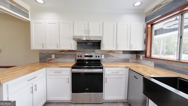 kitchen featuring stainless steel appliances, wooden counters, crown molding, under cabinet range hood, and tasteful backsplash