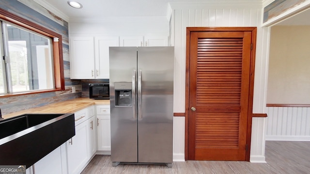 kitchen with stainless steel refrigerator with ice dispenser, light wood-style floors, a sink, white cabinetry, and ornamental molding