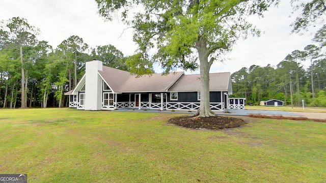 view of front facade with a front lawn, a chimney, metal roof, and view of wooded area