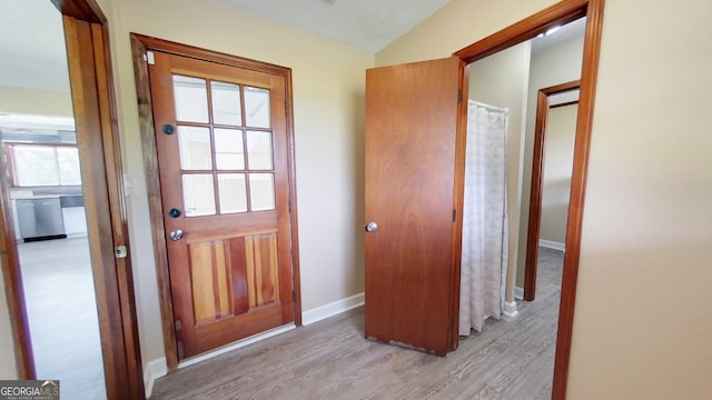 doorway to outside featuring light wood finished floors, baseboards, and lofted ceiling