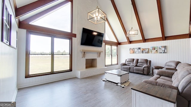 living area featuring high vaulted ceiling, beam ceiling, wood finished floors, a fireplace with raised hearth, and a chandelier