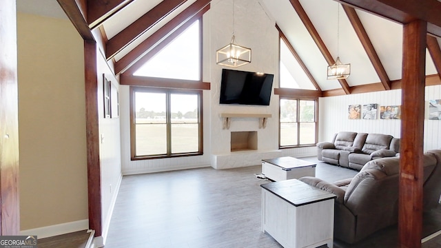 living area featuring a chandelier, beamed ceiling, wood finished floors, high vaulted ceiling, and a fireplace with raised hearth