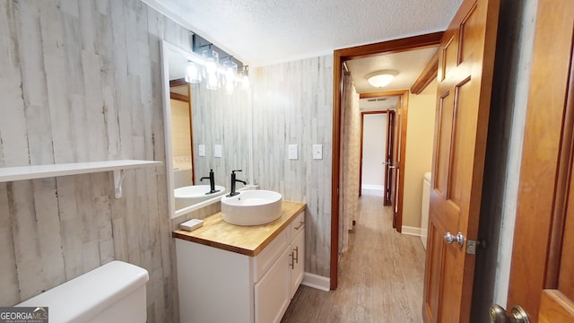 bathroom with wood finished floors, toilet, vanity, a textured ceiling, and wood walls