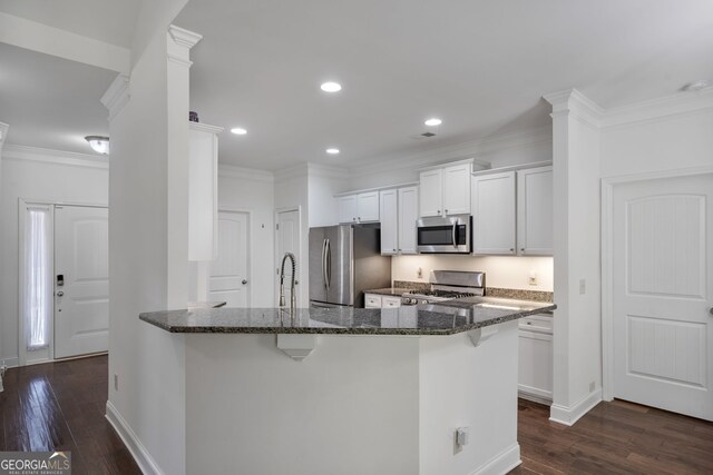 328 Spence Cir, Ball Ground, GA 30107 - kitchen featuring appliances with stainless steel finishes, dark stone counters, a kitchen breakfast bar, dark wood finished floors, and ornamental molding