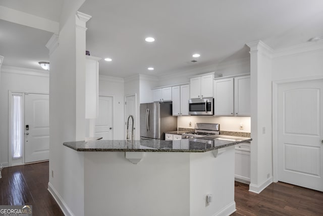 328 Spence Cir, Ball Ground, GA 30107 - kitchen featuring appliances with stainless steel finishes, dark stone counters, a kitchen breakfast bar, dark wood finished floors, and ornamental molding