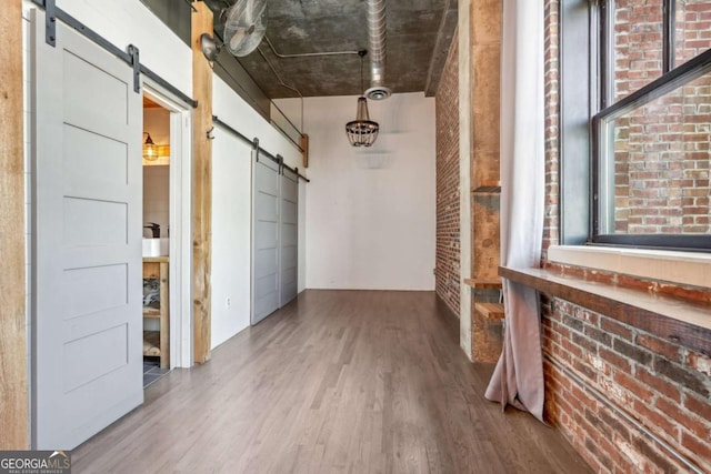 hallway featuring brick wall, a barn door, and wood finished floors