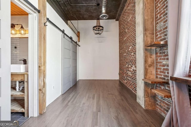 corridor with brick wall, light wood finished floors, a notable chandelier, and a barn door