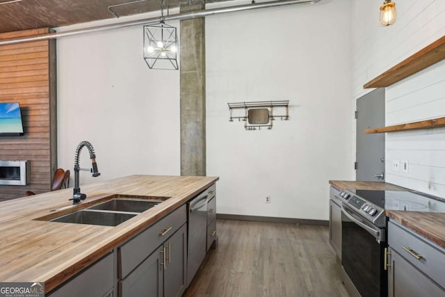kitchen featuring a brick fireplace, dishwasher, a sink, wooden counters, and a chandelier