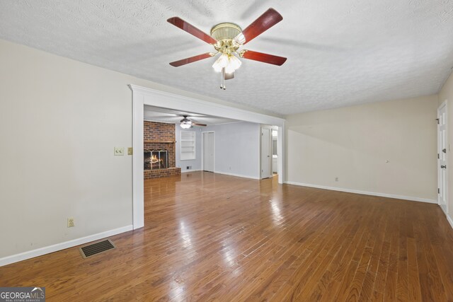 unfurnished living room featuring a textured ceiling, visible vents, a brick fireplace, ceiling fan, and wood-type flooring