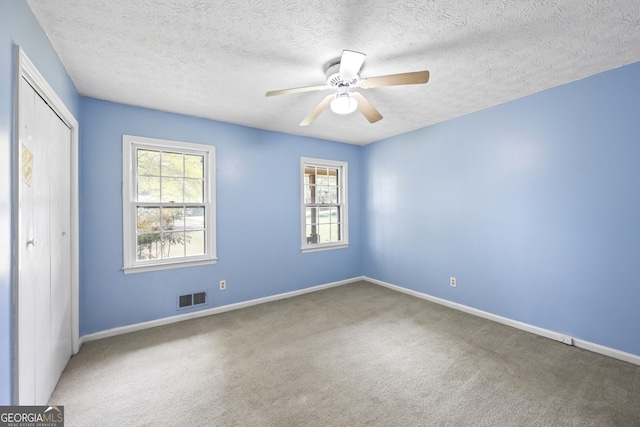 carpeted empty room featuring a textured ceiling, ceiling fan, baseboards, and visible vents