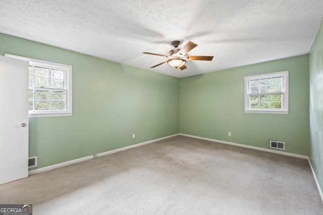 empty room featuring a textured ceiling, carpet flooring, a ceiling fan, and visible vents