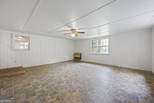 empty room with a ceiling fan, heating unit, and stone finish flooring