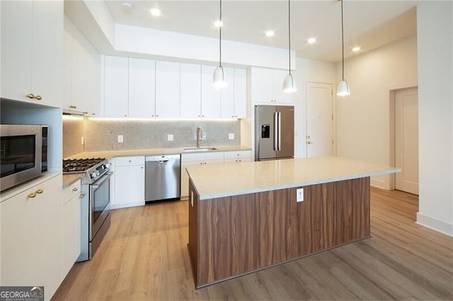 kitchen with white cabinets, a sink, light wood finished floors, stainless steel appliances, and a kitchen island
