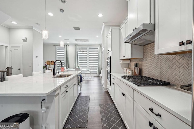 kitchen featuring under cabinet range hood, appliances with stainless steel finishes, light countertops, a sink, and backsplash