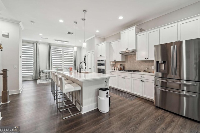 kitchen featuring light countertops, backsplash, under cabinet range hood, appliances with stainless steel finishes, and a sink