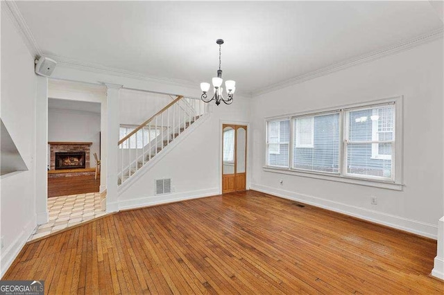 873 Monroe Cir NE, Atlanta, GA 30308 - unfurnished living room with an inviting chandelier, a fireplace, stairway, crown molding, and wood-type flooring