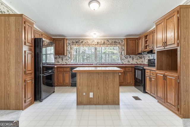 kitchen featuring a textured ceiling, black appliances, light floors, exhaust hood, and a kitchen island