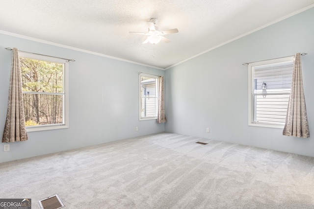 carpeted empty room featuring a ceiling fan, crown molding, visible vents, and a healthy amount of sunlight