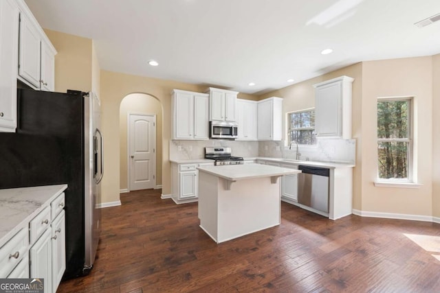 3892 Trillium Wood Trl, Snellville, GA 30039 - kitchen featuring appliances with stainless steel finishes, a kitchen island, light countertops, arched walkways, and dark wood-style flooring