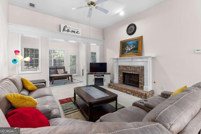carpeted living area with a brick fireplace, visible vents, and a ceiling fan