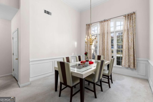 carpeted dining space featuring crown molding, a decorative wall, visible vents, wainscoting, and a notable chandelier
