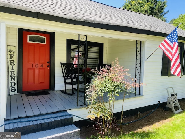 entrance to property with a shingled roof and a porch