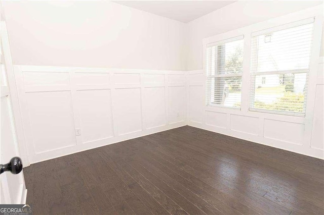 empty room with a decorative wall, dark wood-style flooring, and wainscoting