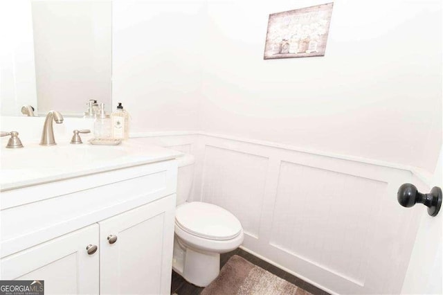 bathroom with a decorative wall, a wainscoted wall, vanity, and toilet